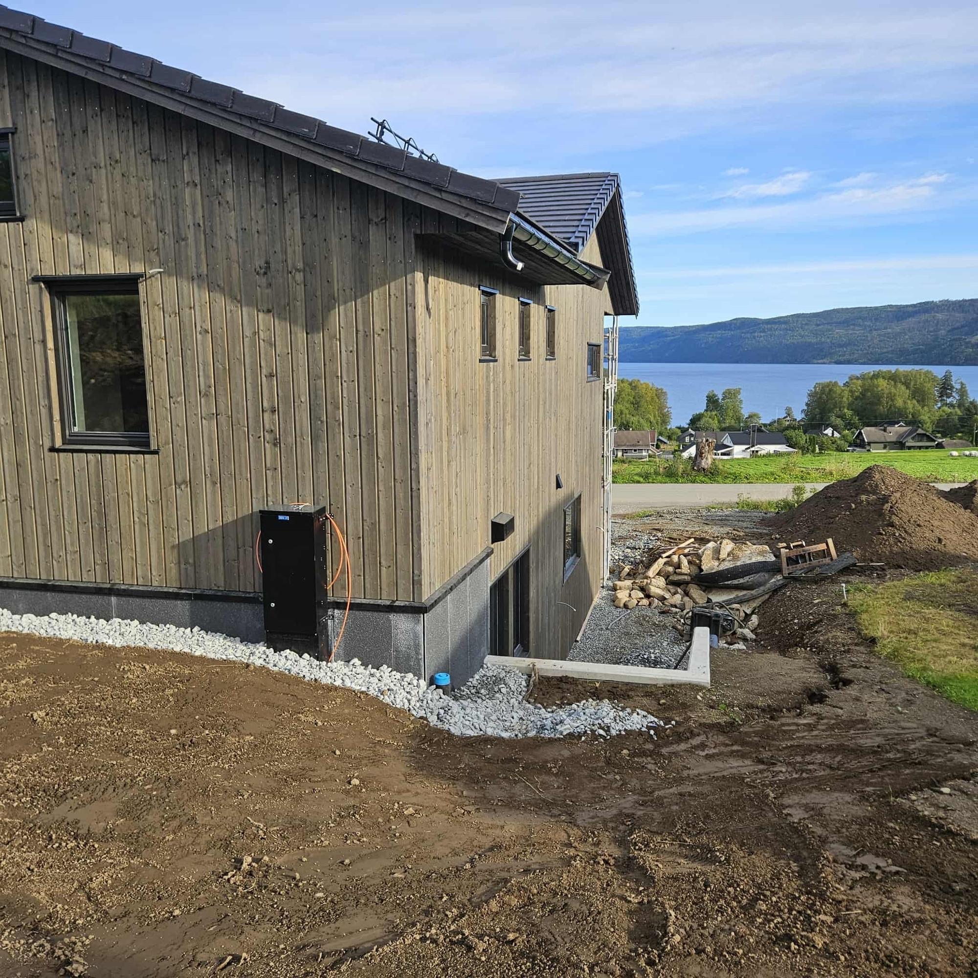 Nytt hus kledd i grå trepanel, med fjorden og åsene bak