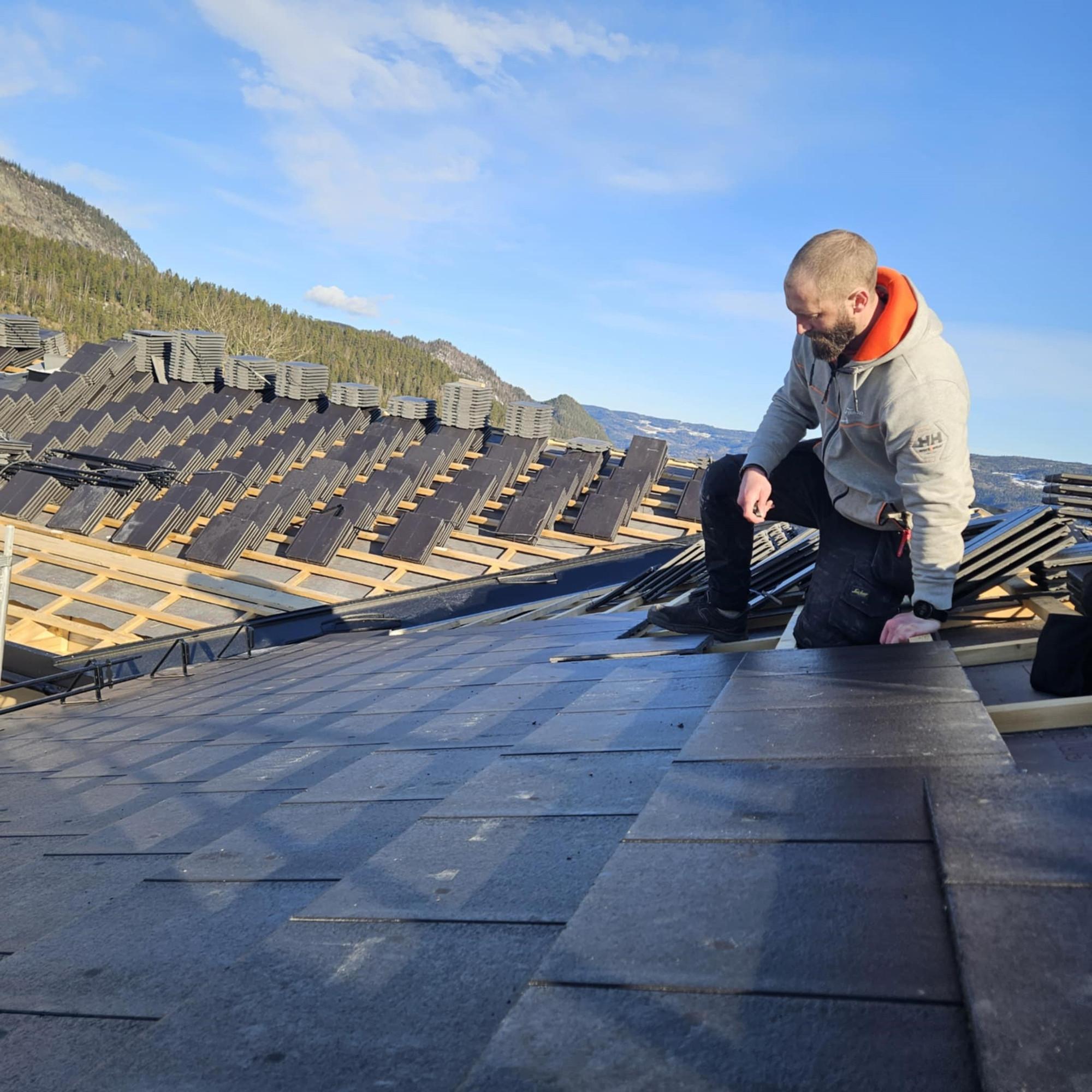 Tømrer som legger takpapp på et tak, med fjellet bak